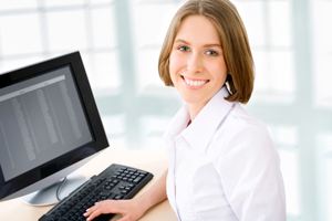 Picture of a woman sitting at a desk on the computer smiling.