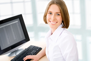 Picture of a smiling woman sitting at a desk on the computer.