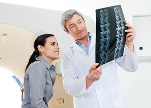 Female patient sitting down while a male Physician holds up X-Ray Images