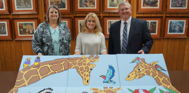 Georgia-Pacific, LLC. has made a donation of artwork to D.W. McMillan Memorial Hospital. There is two females and a male holding up this large painting of two Giraffes and birds.